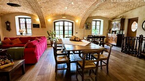 A spacious living room with a red sofa, wooden dining table, and arched windows. - Beautifully restored farmhouse with pool immersed in the greenery (MAGLIANO ALFIERI)