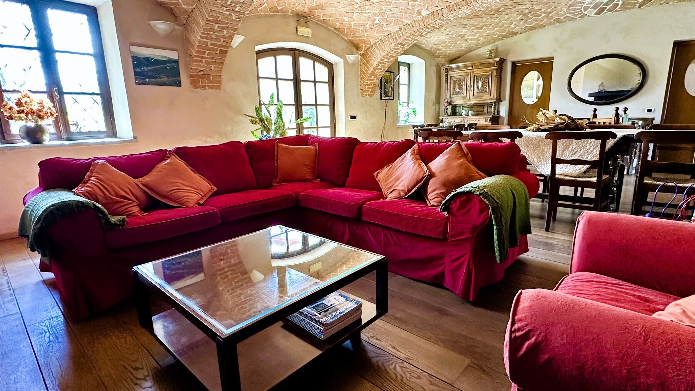 Ein Wohnzimmer mit einem roten Ecksofa, einem Glastisch, Holzboden und einer Ziegeldecken.
