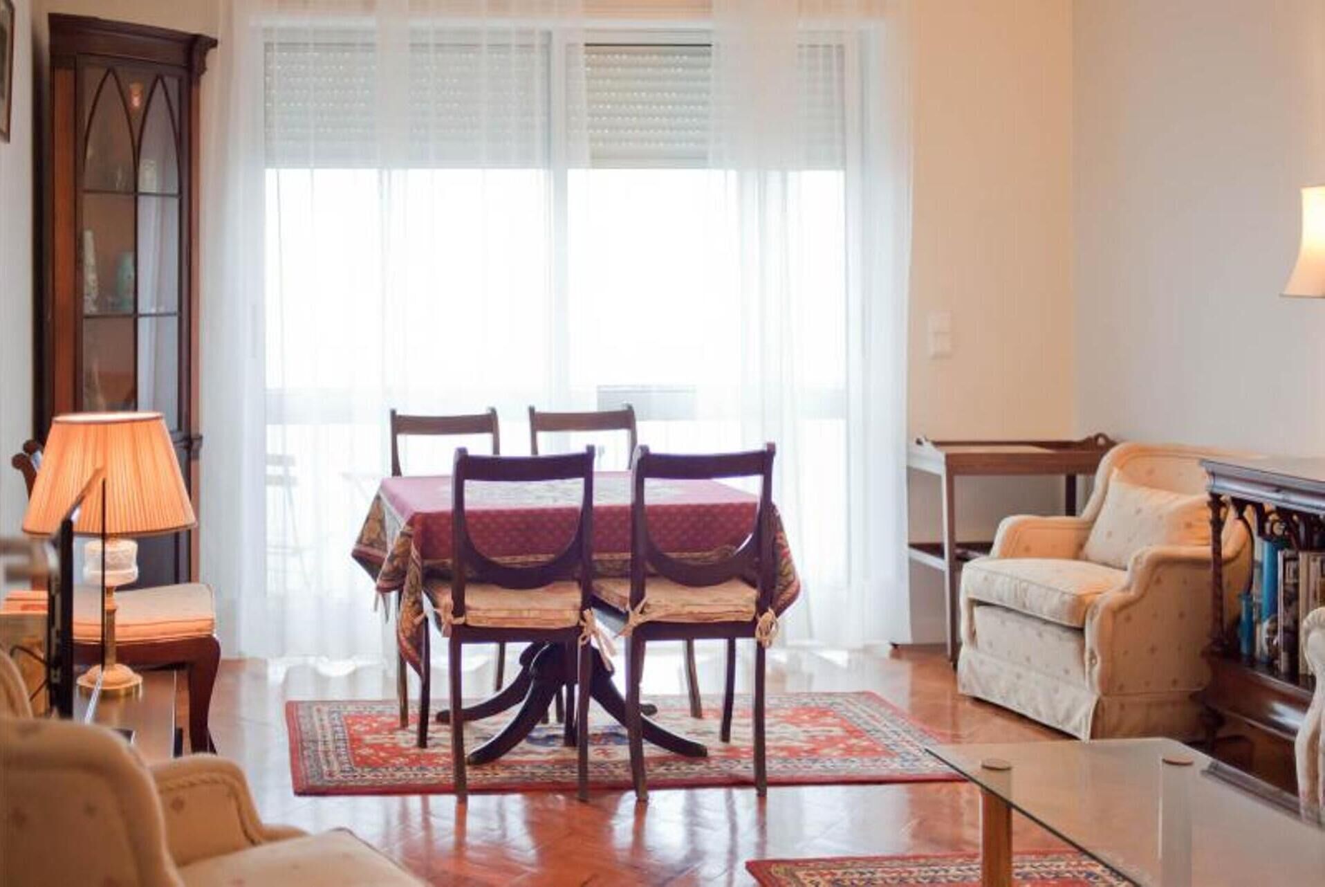 A dining area with a table and chairs, a sofa, a lamp, and a window with blinds.