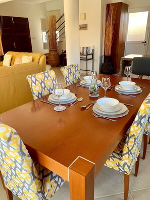 Un coin repas avec une table en bois dressée pour quatre personnes, entourée de chaises à motifs.