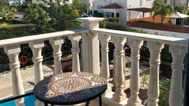 A balcony with a tiled table and chair, a pool, and a view of neighboring houses and greenery. - Private Villa With Large Private Pool Situated In Coral Bay, Paphos, Cyrprus (coral bay)