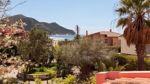 Vista sulla costa con una montagna sullo sfondo, una spiaggia e un giardino con alberi in fiore.