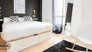 Ein modernes Schlafzimmer mit einem großen Bett, einem kleinen weißen Stuhl, einem schwarzen Teppich und einem Fenster mit transparenten Vorhängen.
