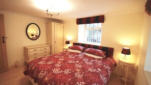 Een slaapkamer met een groot bed, een kaptafel, een spiegel, een raam met gordijnen en twee bedlampen.