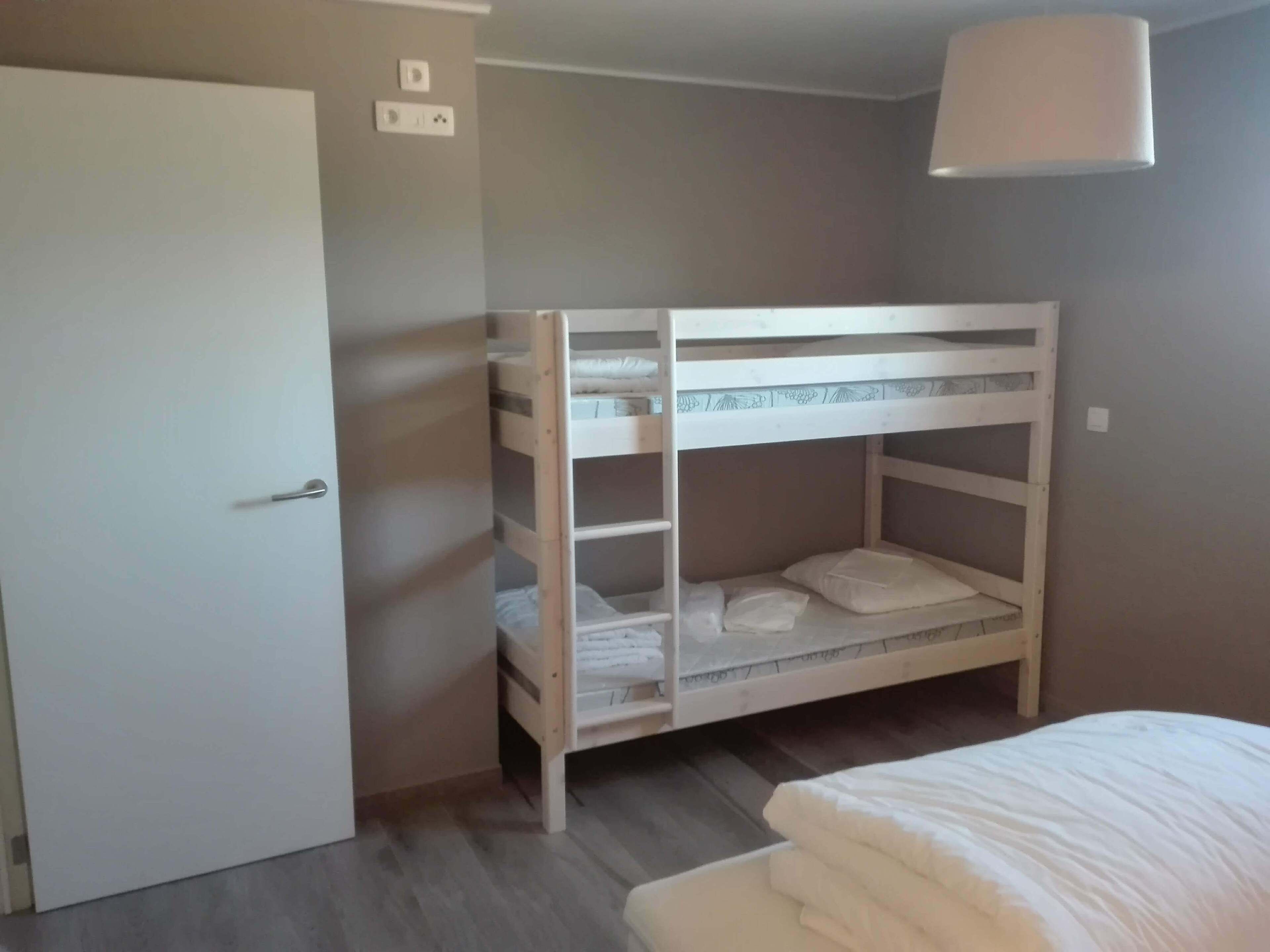 A bunk bed with a white headboard, a door to the left, and a light fixture above.