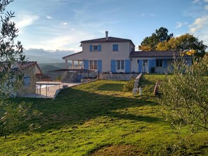 Una casa de dos pisos con techo inclinado, escaleras de piedra y un patio cercado.