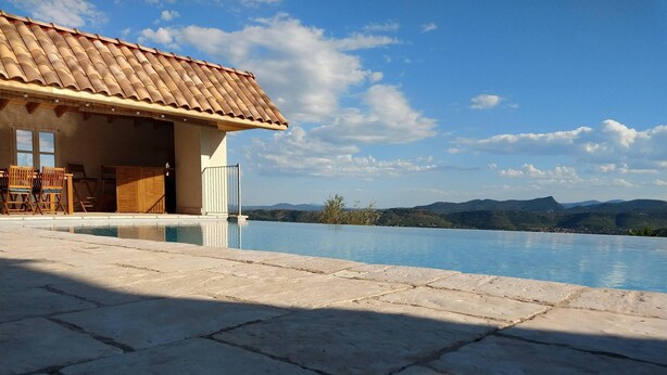 Piscina com vista para montanhas, um edifício com telhado em azulejos e área de varanda.