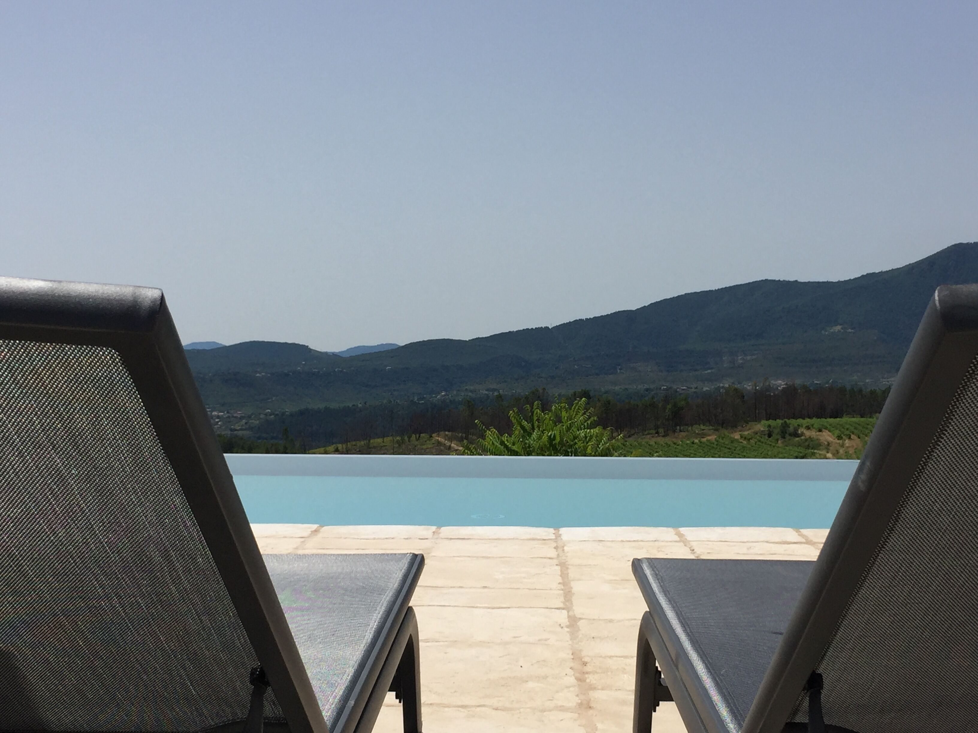 Two lounge chairs facing a swimming pool with a view of mountains in the background.
