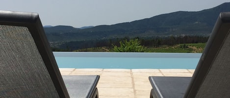 Two lounge chairs facing a swimming pool with a view of mountains in the background.
