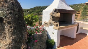 A stone-built outdoor kitchen with a chimney, surrounded by greenery and a large rock. - Villa with private pool (arzachena)