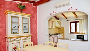 A dining area with a table and chairs, a cabinet with glass doors, and a kitchen visible through an archway. - Villa with private pool (arzachena)