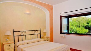 A bedroom with a bed, two bedside tables, a window with a view of greenery, and a wall with a decorative arch. - Villa with private pool (arzachena)