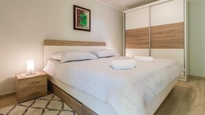 Una cama bien hecha con un cabecero de madera, una mesita de noche con una lámpara y un cuadro enmarcado en la pared.