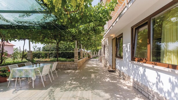 Un espacio de estar al aire libre cubierto con una mesa, sillas, un muro de piedra y un edificio con ventanas grandes.