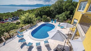 Una piscina con sillones de descanso y sombrillas, rodeada de árboles y vistas al mar.