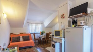 Una habitación compacta con cama, una pequeña mesa de comedor, una kitchenette con microondas, cafetera y televisión.
