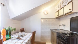 Cocina compacta con estufa, pileta y salpicadero de azulejos. Hay una mesa de comedor con mantel de encaje y sillas.