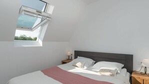 Une chambre avec un puits de lumière, un lit avec des oreillers, une table de chevet avec une lampe et une commode avec une lampe.