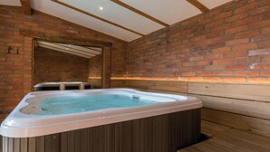 Un bain à remous dans une pièce dotée de bancs en bois et d’un mur en briques.