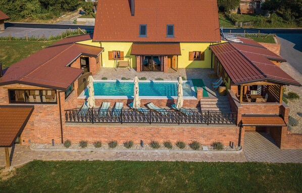Una casa de dos pisos con piscina, un patio cubierto y fachada de ladrillo.