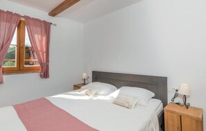 Un dormitorio con una cama, dos mesitas de noche con lámparas, un ventanal con cortinas y una viga de techo de madera.