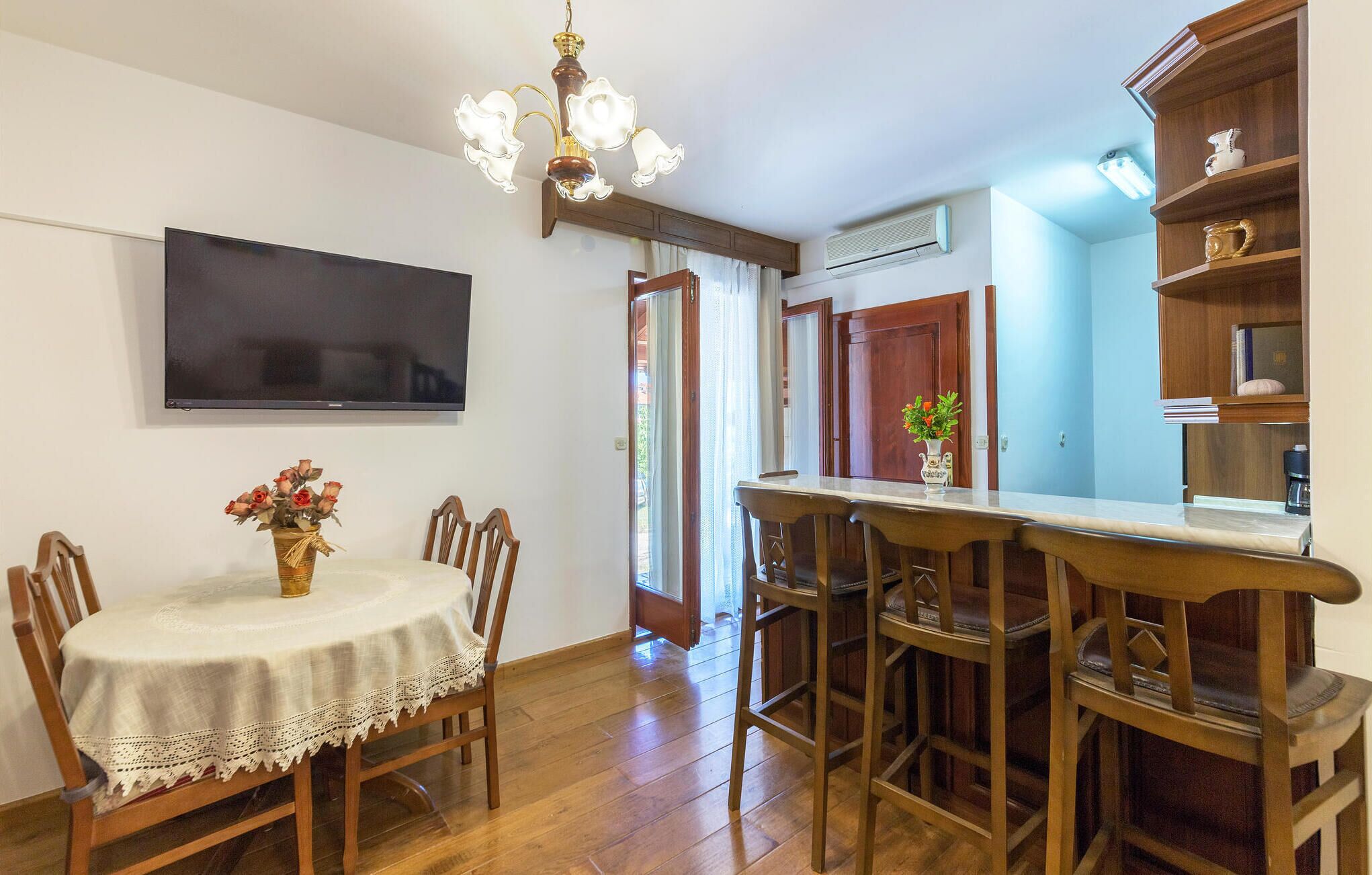Uma sala de jantar com uma mesa e cadeiras, uma televisão na parede e um lustre.