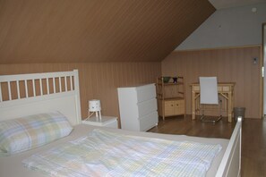 A bedroom with a bed, a nightstand, a dresser, a desk, and a chair.
