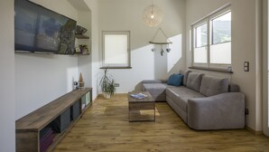 A modern living room with a large flat-screen TV, a wooden coffee table, a grey sofa, and a hanging light fixture. - Welcome to the Millau holiday bungalow in the beautiful Zillertal (Schlitters)