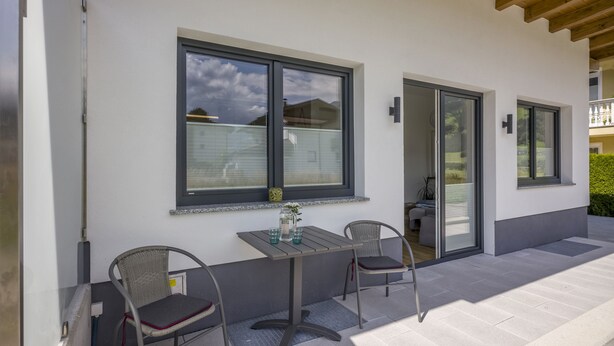 A modern patio with a table and two chairs, large windows, and a wooden ceiling. - Welcome to the Millau holiday bungalow in the beautiful Zillertal (Schlitters)