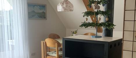 Ein gemütliches Zimmer mit einem Holzstuhl, einem Tisch, einem schwarzen Herd und einem Fenster mit durchsichtigen Vorhängen.