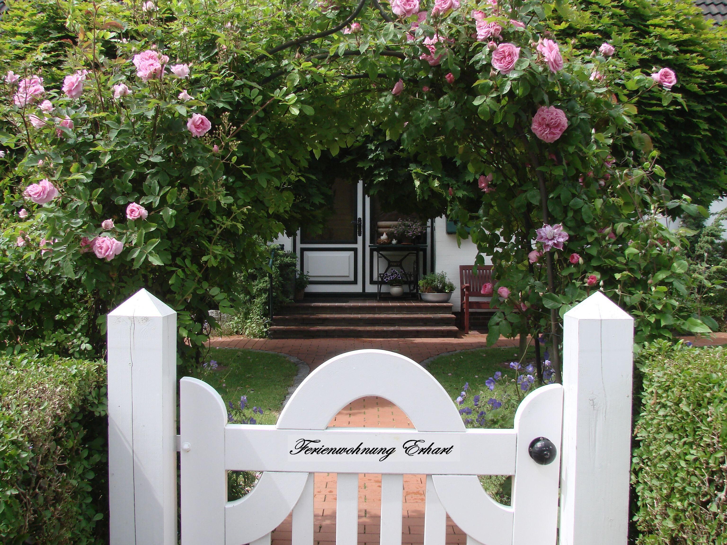 A white gate with the inscription "Ferienwohnung Erhart" leading to a house with a white door and steps.