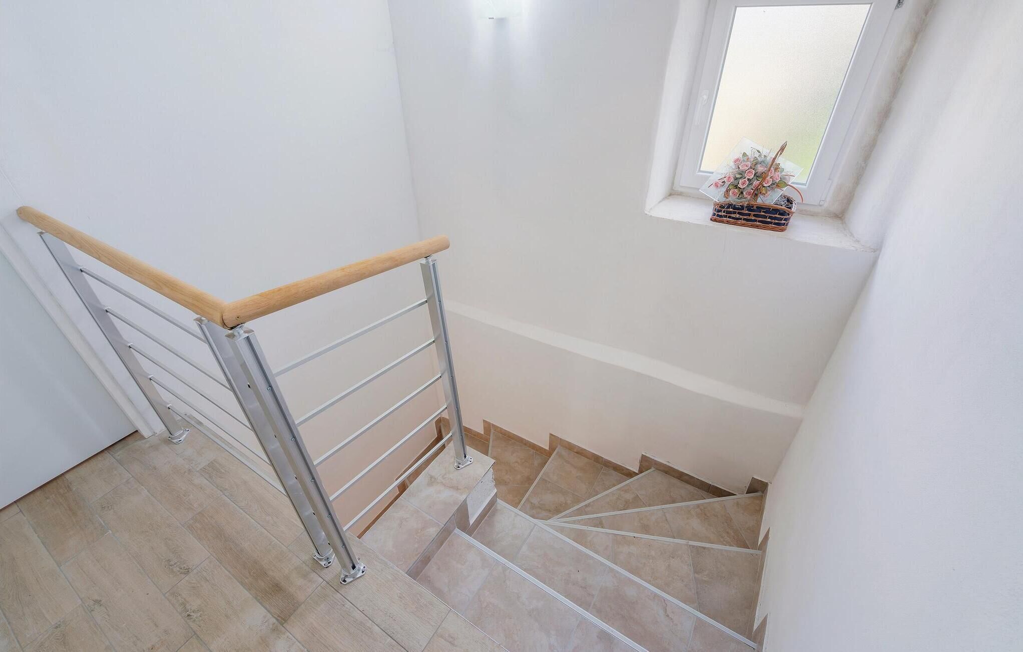 Una escalera con barandilla de madera y balaustradas de metal, que conduce a un rellano con un ventanal pequeño.
