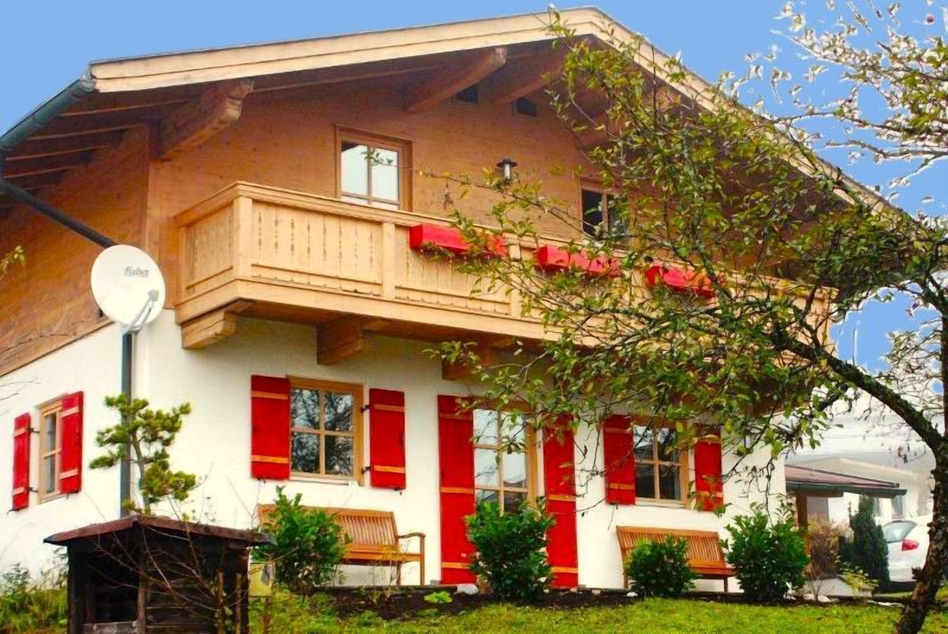 Un chalet traditionnel doté d’un balcon, de volets rouges et d’une antenne parabolique.