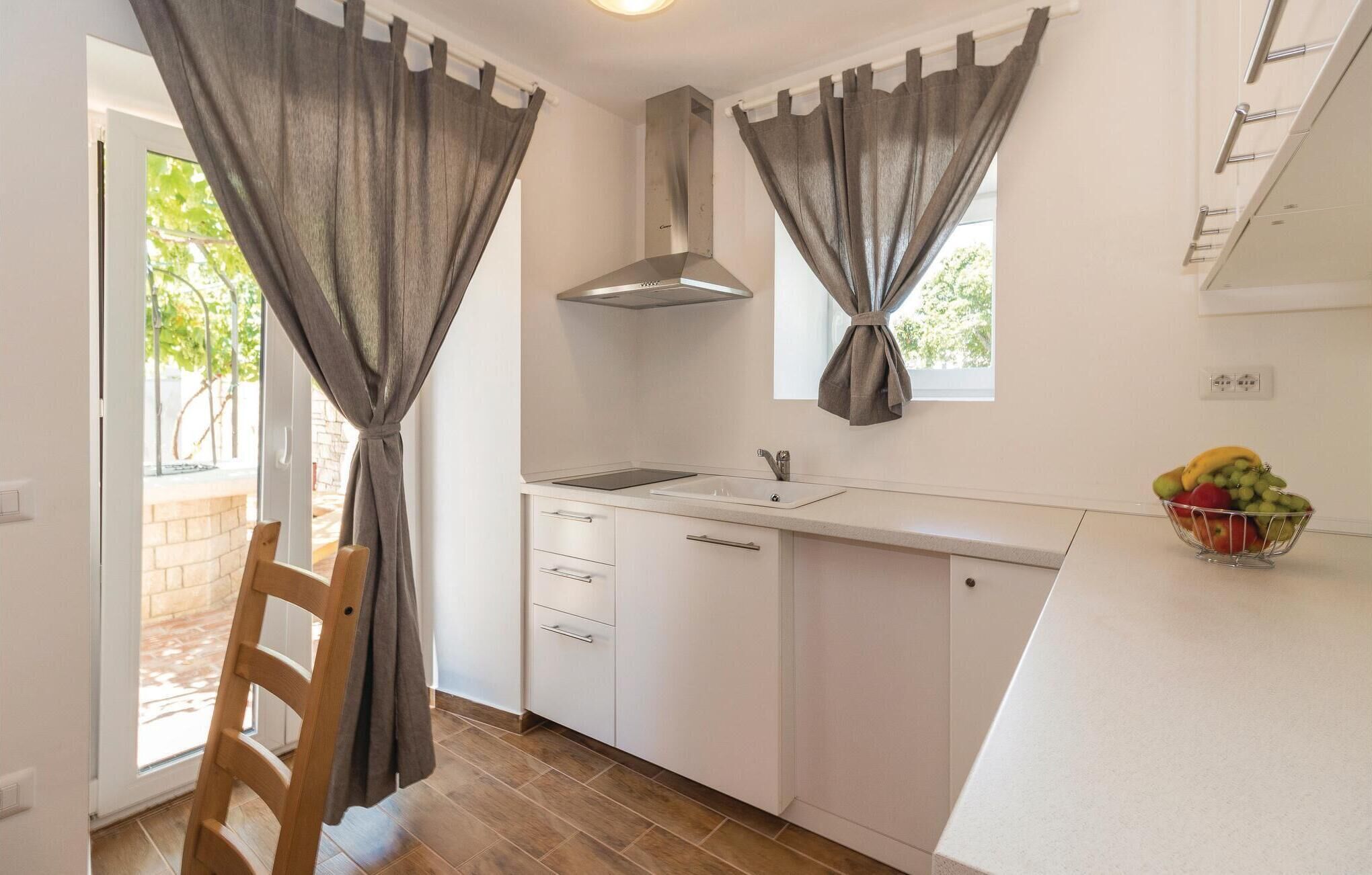 A modern kitchen with white cabinets, a stainless steel sink, and a window with grey curtains.