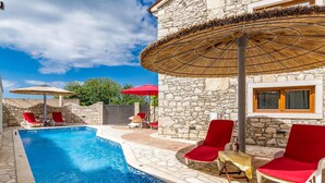 A pool area with stone walls, red lounge chairs, and thatched umbrellas.