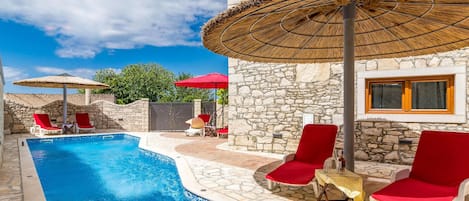 A pool area with stone walls, red lounge chairs, and thatched umbrellas.
