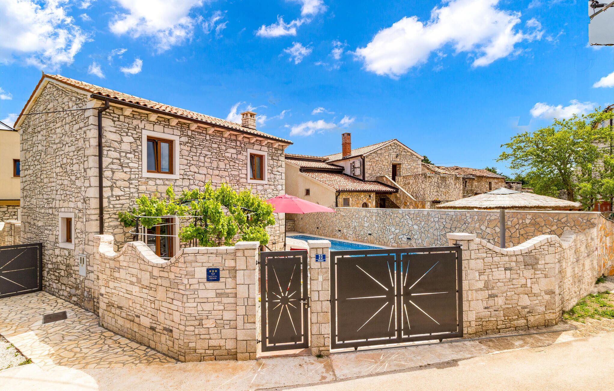 A stone building with a tiled roof, a gated entrance, and a small pool area.