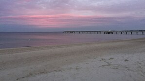 A beach with a pier extending into calm waters under a cloudy sky.