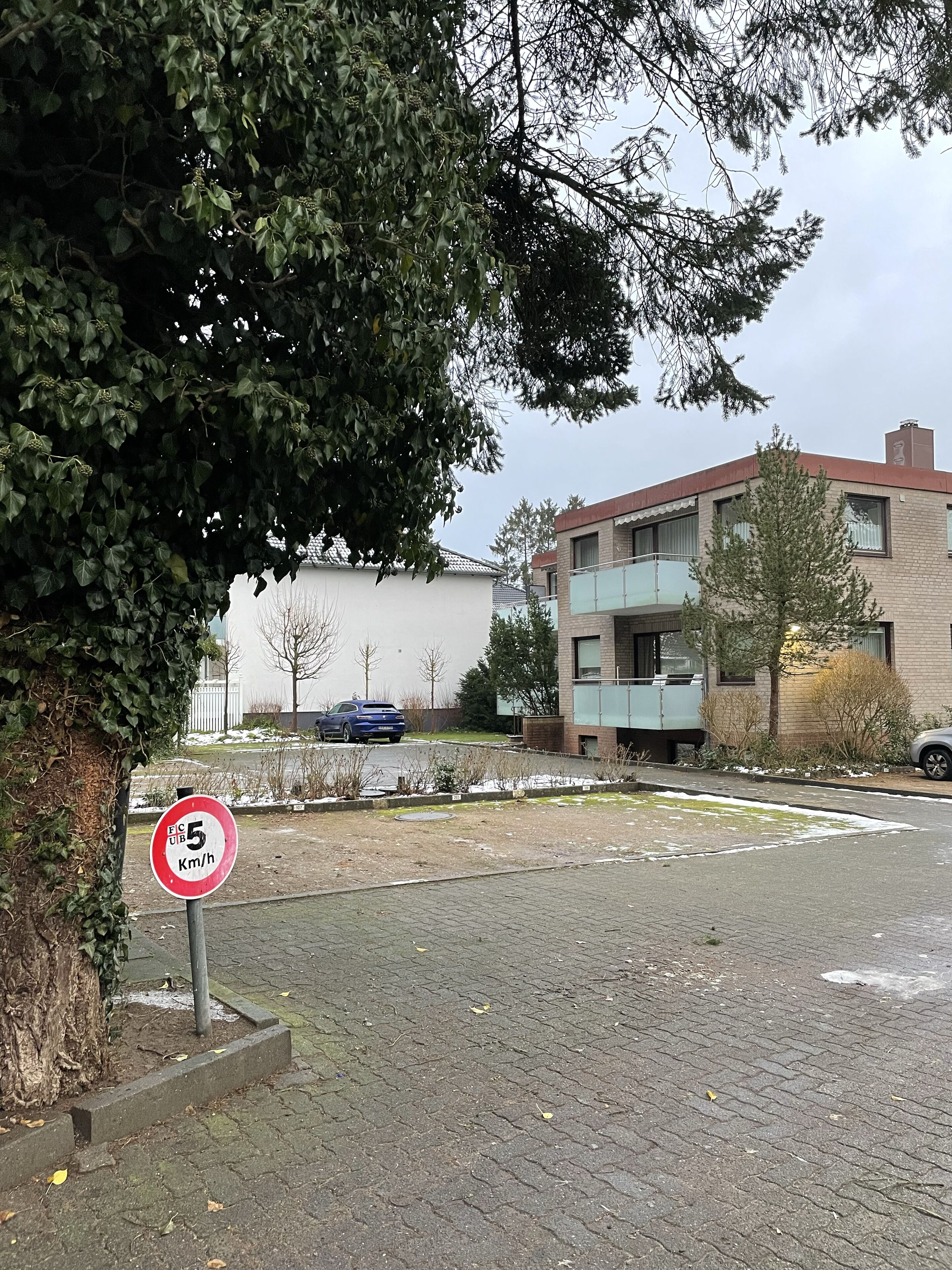 Ein Wohngebiet mit Geschwindigkeitsbegrenzung auf 5 km/h, einer asphaltierten Straße und einem mehrstöckigen Gebäude mit Balkonen.