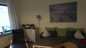 A living room with a sofa, two chairs, a coffee table, and a desk with speakers.