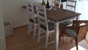 A dining area with a wooden table and white chairs, a hanging light fixture, and a painting on the wall.