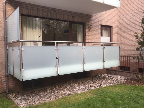 A modern building with a glass balcony, a brick facade, and a small garden area with pebbles and grass.