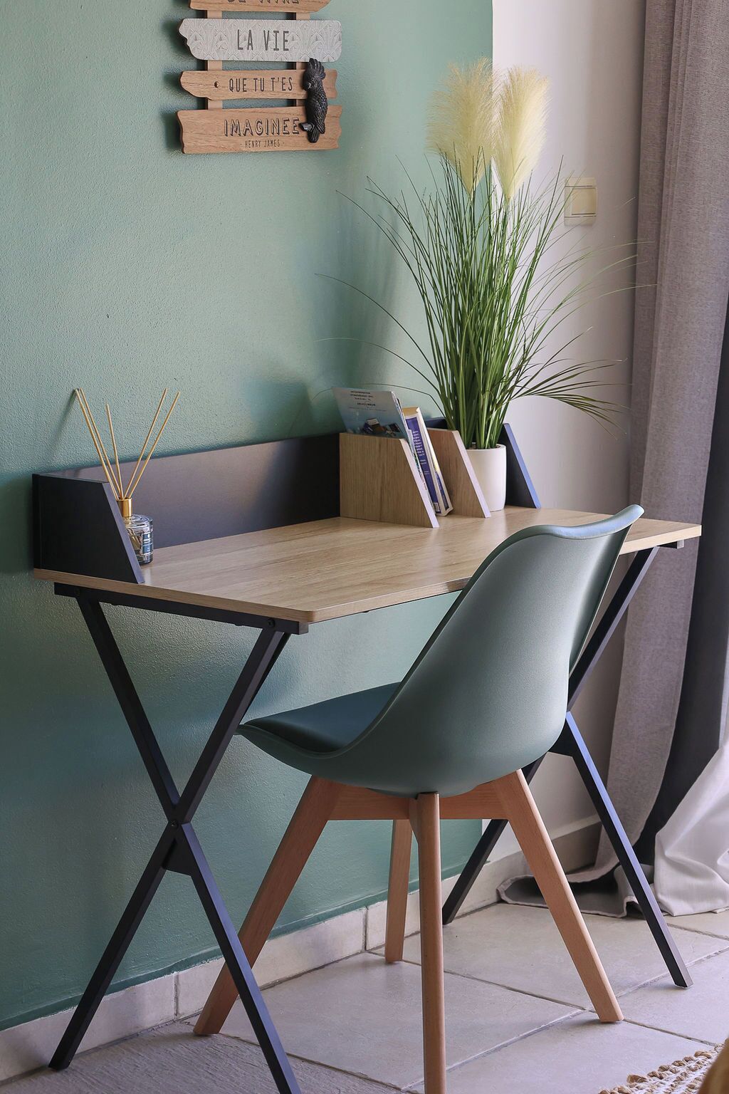 Ein modernes Zimmer mit Schreibtisch aus Holz, zwei Stühlen, einem Topfpflanzen und einem an der Wand befestigten Schild mit motivierenden Sprüchen.