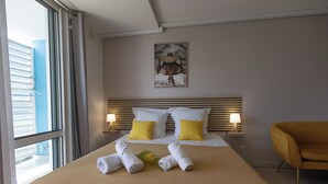 Een hotelkamer met een bed, twee bedlampen, een hoofdbord, een schilderij, een stoel en handdoeken op het bed.