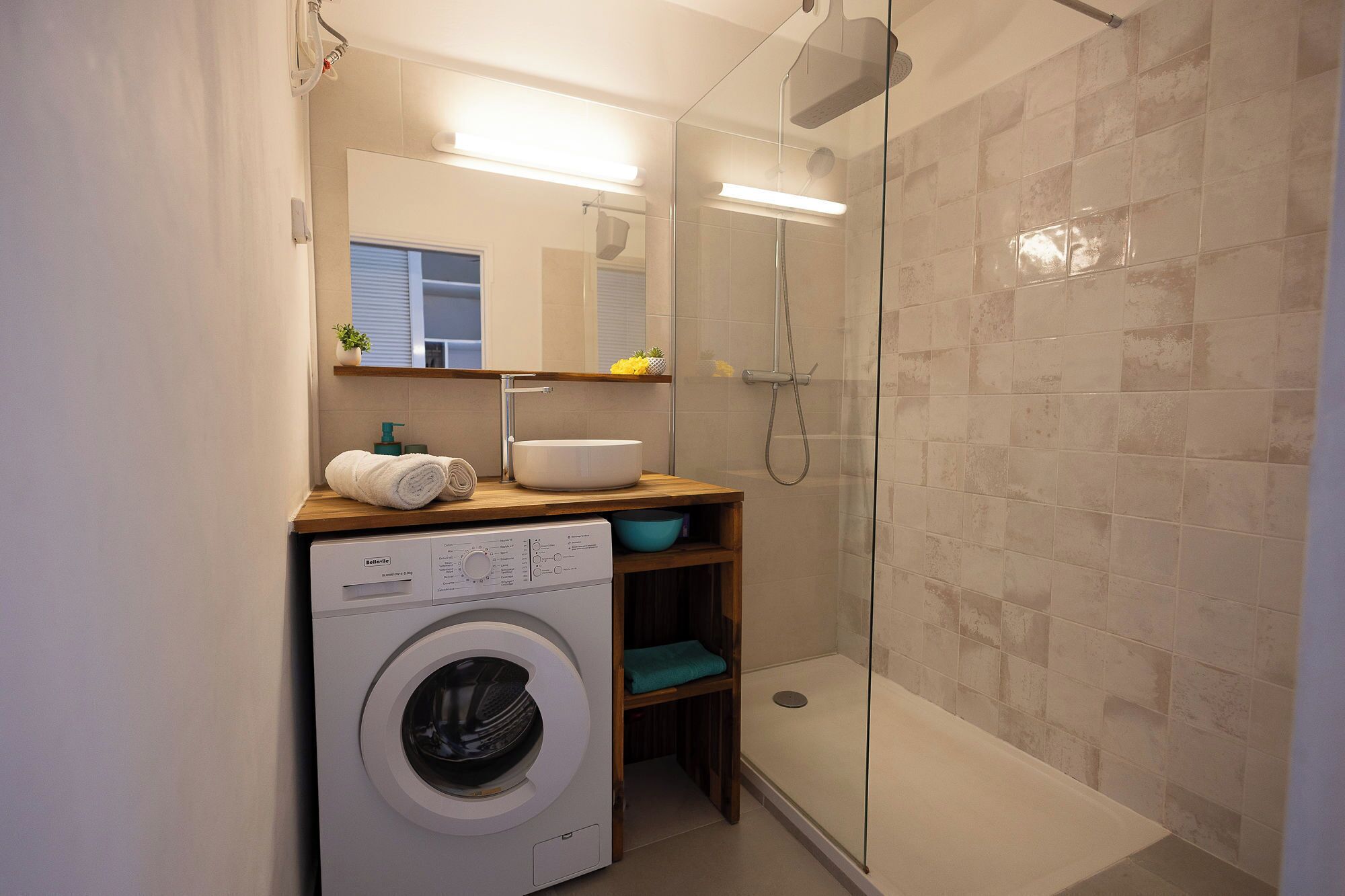 A compact bathroom with a washing machine, a sink, and a glass-enclosed shower.