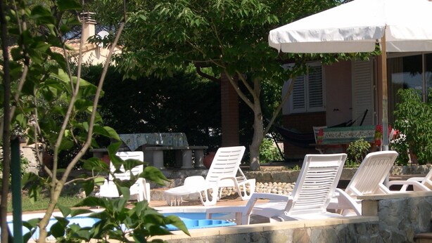 A poolside area with white lounge chairs and a white umbrella.
