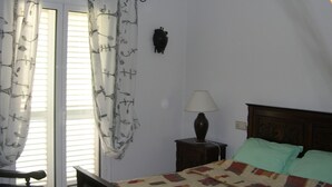 A bedroom with a bed, a nightstand, a lamp, a chair, and a window with curtains.