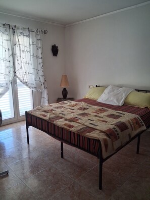 A bedroom with a bed, a nightstand with a lamp, a window with curtains, and a wall-mounted decoration. - A nice house in a protected environment for 1/2 hour from Barcelona (Santa Coloma de Farners)