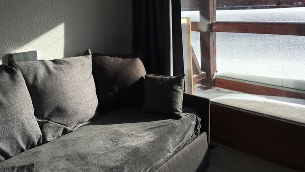 Una habitación con un sofá gris y una ventana que da a un paisaje nevado con un telesilla.