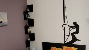 Une chambre à coucher comprenant un lit, un ventilateur de plafond, une étagère fixée au mur avec des livres et un élément décoratif mural.